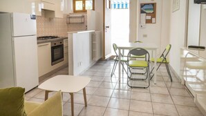 A compact kitchen with a refrigerator, stove, oven, and a dining area with a table and chairs. - M377 - Marcelli, two-room apartment with external courtyard and parking (Marcelli)