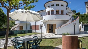 Ein weißes Gebäude mit einer gewölbten Fassade, einer Treppe und einer überdachten Außenbereich-Sitzgelegenheit mit Stühlen und einem Sonnenschirm.