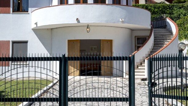 Ein weißes Gebäude mit geschwungenem Eingang, einer Treppe und einem Metallgitter.