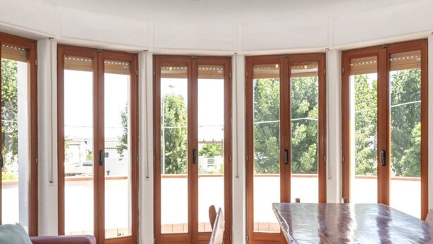 Una habitación con un banco de madera y un sofá, puertas de cristal grandes que dan a un área exterior, y vistas a zonas verdes.