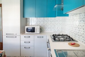 A kitchen with teal cabinets, a microwave, a gas stove, and a tiled backsplash.