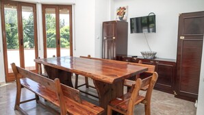 Un comedor con una gran mesa de madera y bancos, un televisor montado en la pared y un armario con un cuenco decorativo.