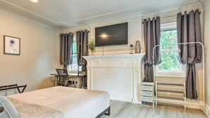 A hotel room with a bed, a desk, a flat-screen TV, a fireplace, and a window with curtains.
