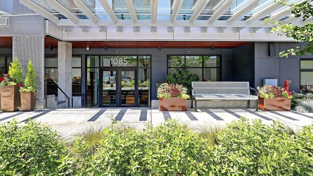 A modern building entrance with a glass door marked "1085", outdoor seating, and potted plants. - New penthouse unit in downtown Bellevue (Bellevue)