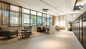 A spacious hotel lobby with a high ceiling, large windows, a seating area with sofas and a coffee table, a reception desk, and a row of lockers. - New penthouse unit in downtown Bellevue (Bellevue)