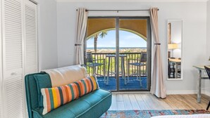 Una habitación con un sofá color turquesa, un cojín a rayas, vista a la playa y un comedor con mesa y sillas.