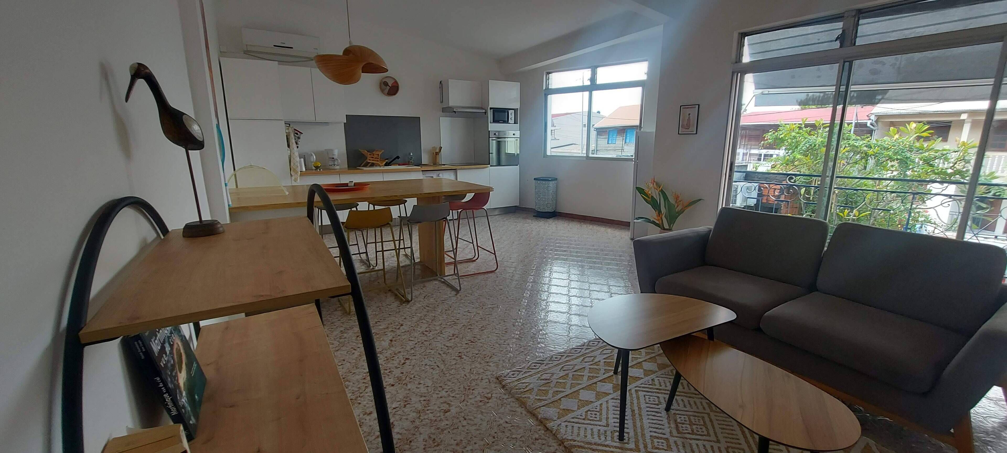 Un salon moderne avec un canapé, une table à manger et des chaises, une petite table basse et, au fond, un coin cuisine.