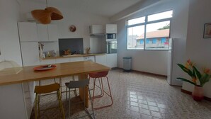 A modern kitchen with a wooden table, chairs, and a window with a view of buildings outside. - Appartement Spacieux et Lumineux à 20m de la Plage ! (Les Anses-d'Arlet)