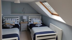 Un dormitorio con dos camas individuales, una mesita de noche con lámpara, un radiador y un tragaluz.