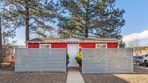 Un bâtiment rouge avec une porte blanche, entouré d’une allée gravillonnée et de deux portails blancs.