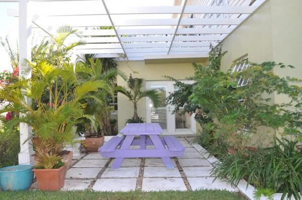 Une terrasse couverte avec un banc violet, entourée de plantes en pot et dotée d’un sol carrelé.