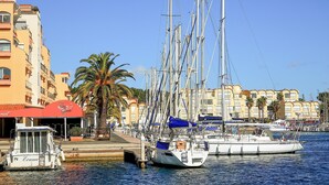 Un puerto deportivo con varios veleros amarrados, una palmera y edificios con balcones.