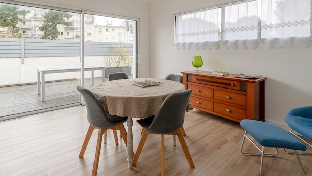 Ein modernes Zimmer mit Esstisch, Stühlen, einer Holzschrank und einem großen Fenster mit Blick auf Gebäude und Bäume.