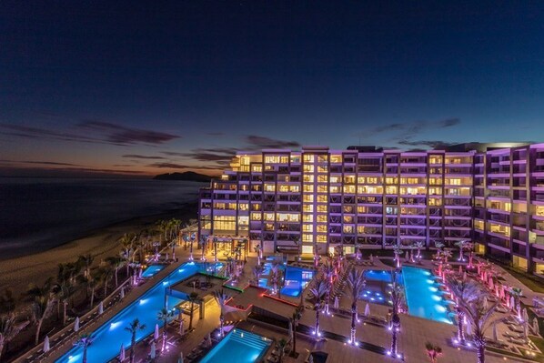 A multi-story hotel with a pool area, surrounded by palm trees and a beach view. - Incredible 2-Bedroom Ocean View Suite at Garza Blanca 5-Star Resort: Los Cabos (Cabo San Lucas)