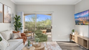Een moderne woonkamer met een bank, fauteuil en salontafel, een balkon met uitzicht op de stad, en een wandgemonteerde televisie.