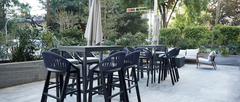 An outdoor patio area with a table and chairs, surrounded by greenery and a view of the city.