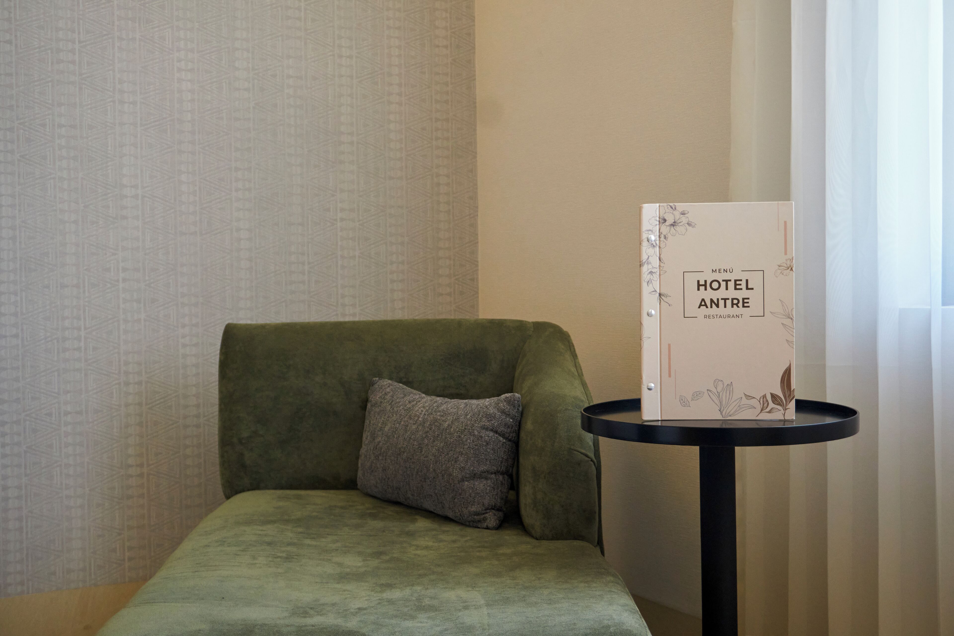 A green sofa with a pillow, a small round table with a menu sign, and a patterned wall.