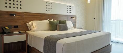 A modern hotel room with a large bed, a nightstand with a phone, and a window with curtains.
