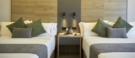 A hotel room with two beds, each with a pillow and a bedside table with a phone and a lamp.