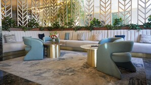 A modern living room with a sectional sofa, two accent chairs, a round coffee table, and a decorative plant arrangement. - Hotel Antré Chapultepec (Guadalajara)
