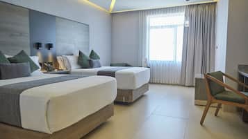Quarto de hotel moderno com duas camas, uma cadeira de madeira e uma janela grande com cortinas.