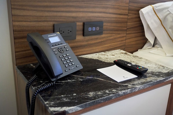 Habitación de hotel con un teléfono, un control remoto y un bloc de notas sobre la encimera.