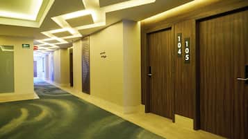 Corredor de hotel com portas de madeira numeradas 104 e 105, carpete verde e teto com iluminação geométrica.