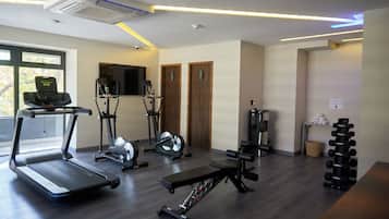 Un gimnasio con cintas de correr, elípticas, una prensa de banca y una estantería con mancuernas.