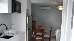 Una cocina compacta con armarios blancos, un microondas integrado y un comedor con sillas y mesa de madera.