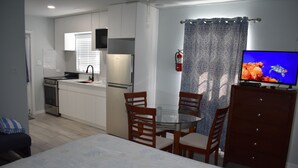 Cocina compacta con refrigerador, estufa y lavamanos. Hay una mesa de comedor con sillas y un televisor sobre un aparador.