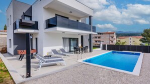 Ett modernt hus i två våningar med en swimmingpool, en uteplats och utsikt över det omgivande området.