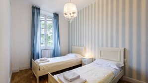 A hotel room with two beds, a chandelier, striped wallpaper, and a window with curtains. - Fabbroni 3 bedrooms in Florence by Mmega (Firenze)