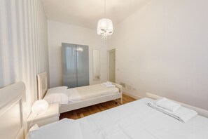 A hotel room with two beds, a wardrobe, a chandelier, and a mirror.