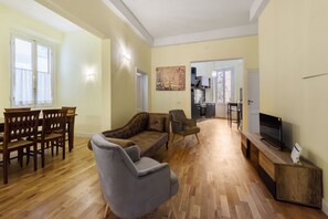 A living room with a wooden floor, a sofa, a TV, and a dining area with chairs and a table.