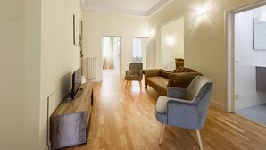 A spacious living area with a wooden floor, a television, a sofa, and a chair. - Fabbroni 3 bedrooms in Florence by Mmega (Firenze)