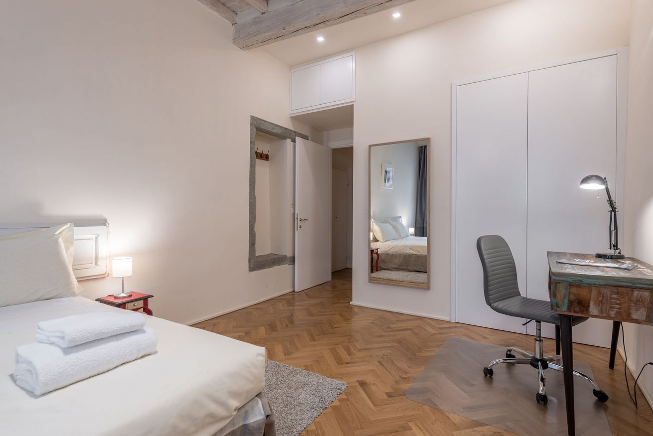 Een slaapkamer met een bed, een bureau, een stoel, een spiegel en een kledingkast.