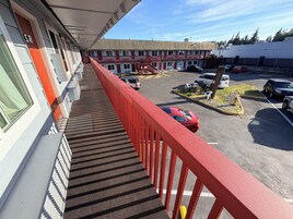 Un hotel con barandal rojo, aparcamiento y un edificio con múltiples ventanales.