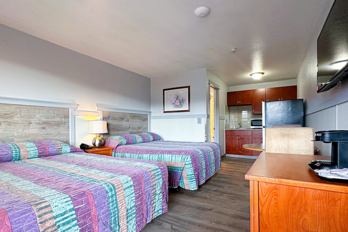 A hotel room with two beds, a desk, a microwave, and a kitchenette.