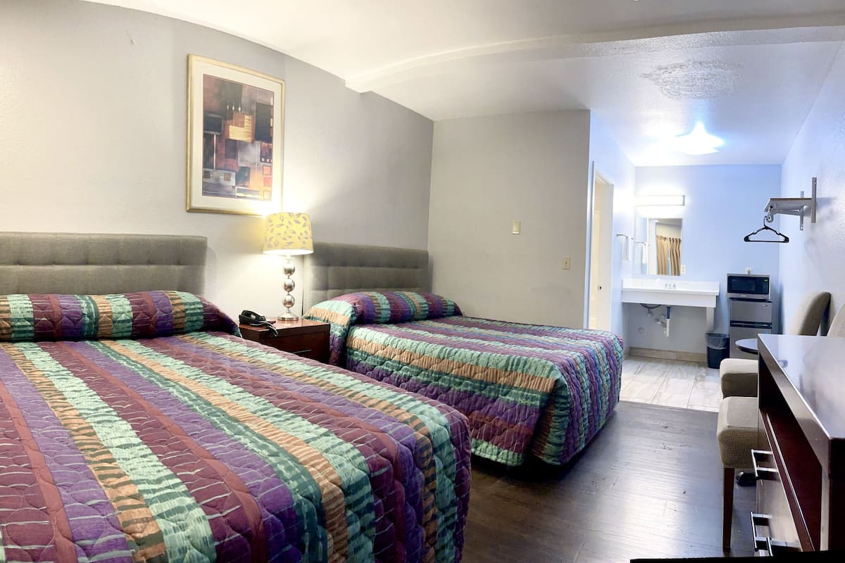 A hotel room with two beds, a desk, a chair, a lamp, and a painting on the wall.