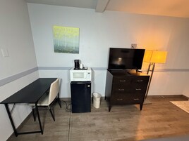 Una habitación compacta con escritorio, silla, microondas, refrigerador, televisor y lámpara.