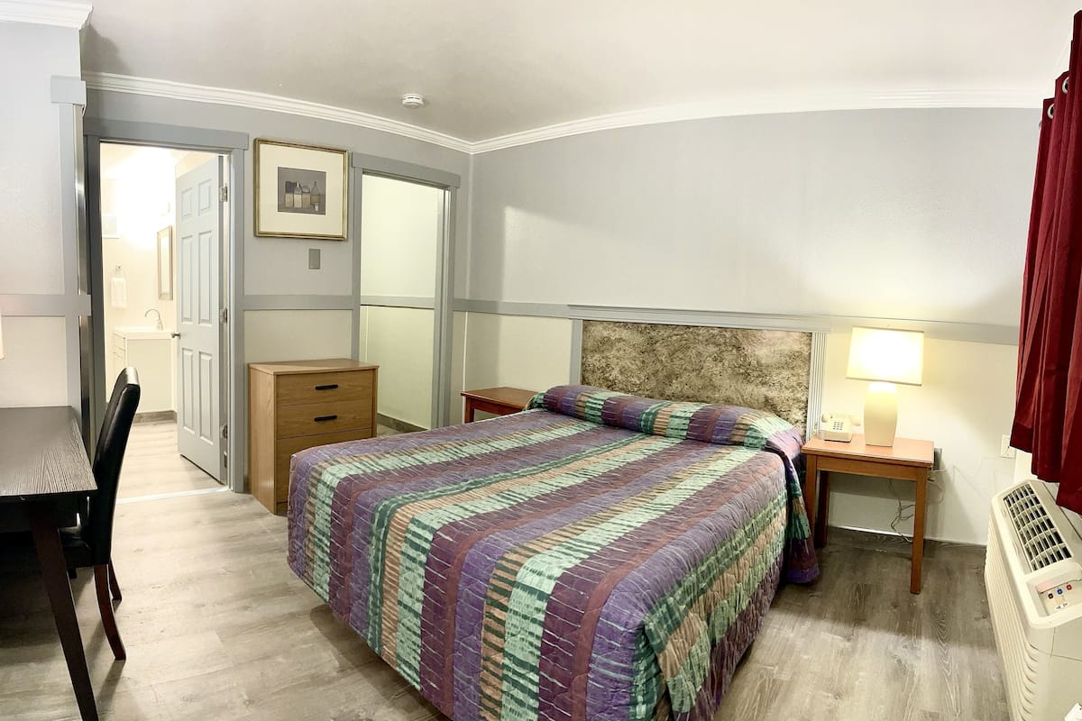 A neatly arranged bedroom with a bed, bedside tables, a desk, and a chair.
