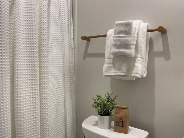Un baño con un perchero blanco, una toalla blanca, una planta en maceta y una bolsa de papel marrón sobre el inodoro blanco.