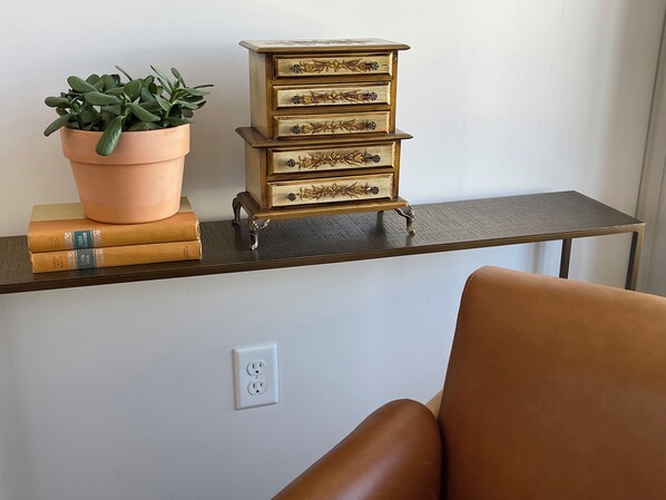 A desk with a stack of books, a potted plant, and a small wooden chest of drawers.