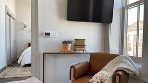 A modern living room with a brown leather armchair, a flat-screen TV mounted on the wall, a potted plant, and a stack of books on a console table. - Hall Building (Aledo)