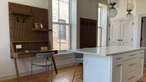 A modern kitchen with a wooden accent wall, a built-in island, and a window with a view of a brick building. - Hall Building (Aledo)