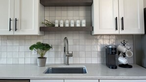 A kitchen with white cabinets, a stainless steel sink, and a coffee machine. - Hall Building (Aledo)