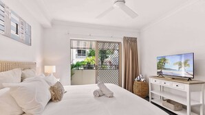 A hotel room with a bed, a TV, a ceiling fan, a balcony with a view, and a white wall. - Luxurious Resort Apartment with 9 Pools and Patio (Westcourt)
