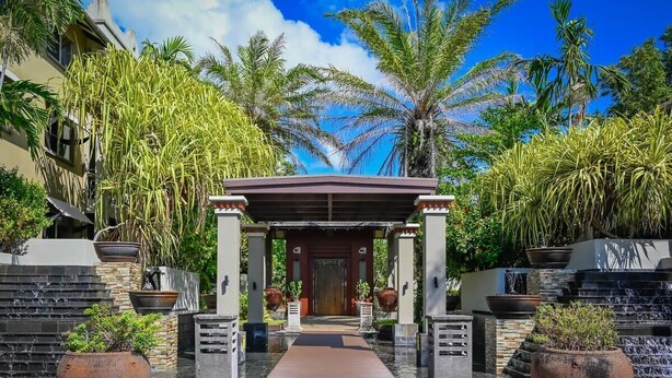 A tropical resort entrance with a covered walkway, palm trees, and potted plants. - Luxurious Resort Apartment with 9 Pools and Patio (Westcourt)
