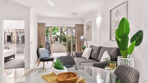 A modern living room with a glass coffee table, grey sofa, and large green plants. - Luxurious Resort Apartment with 9 Pools and Patio (Westcourt)