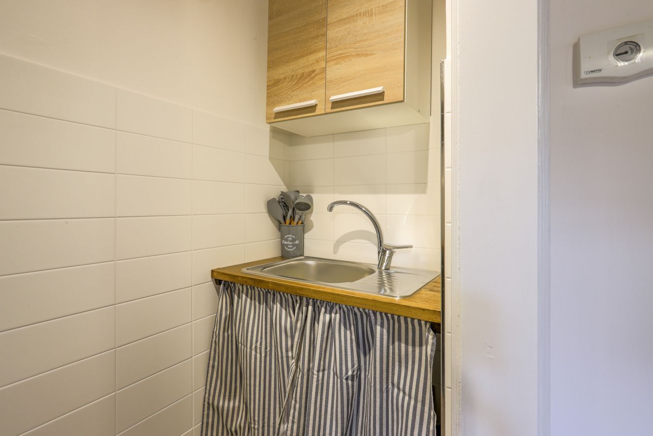 A small kitchen with a wooden countertop, a stainless steel sink, and a striped curtain.